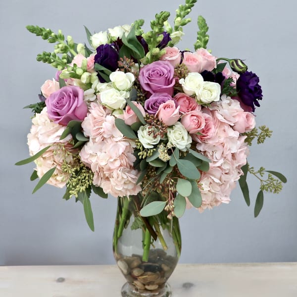 Tall glass vase arrangement with pink hydrangeas, roses, and white and purple accent blooms
