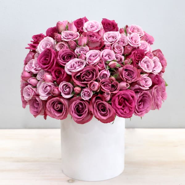 Dome-shaped arrangement of pink and magenta roses in a white cylinder vase