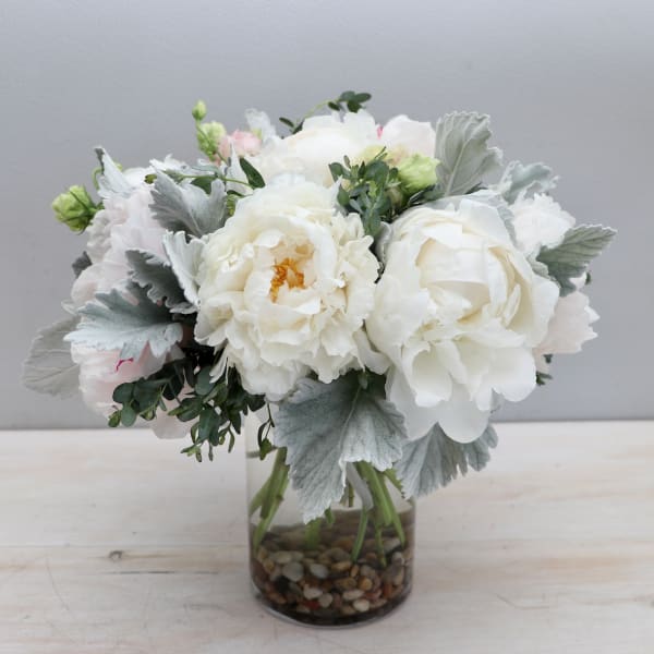 Compact arrangement of white peonies in a glass vase with river stones.