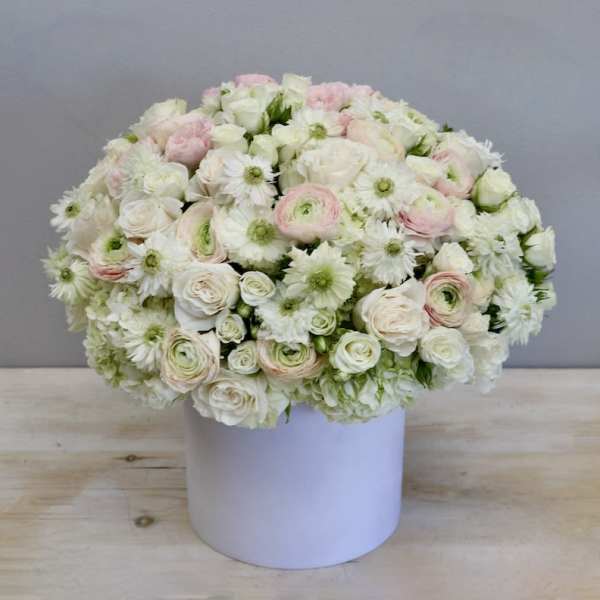 Low round arrangement of white and pale pink flowers in a white cylinder box