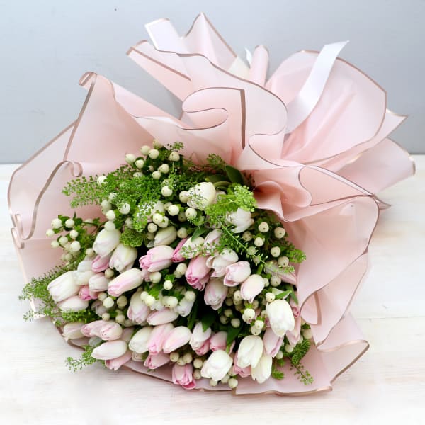 Hand-tied bouquet of white and pale pink tulips with white berries wrapped in ruffled blush paper