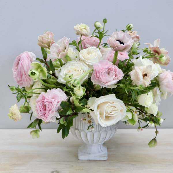 Low arrangement of pink and ivory roses and ranunculus in a white pedestal bowl