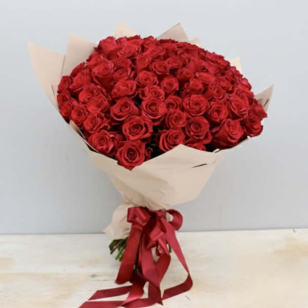 Large bouquet of red roses wrapped in beige paper with a red ribbon bow