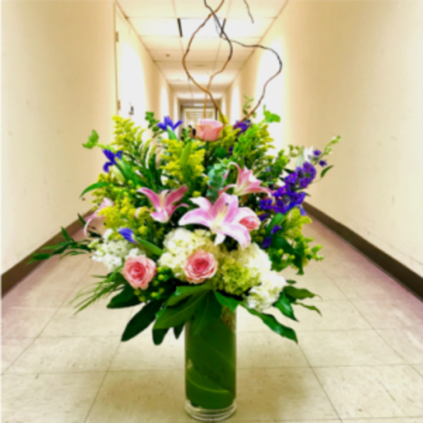Tall mixed flower arrangement in a green vase with pink lilies and roses