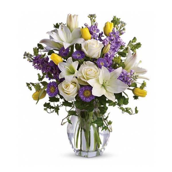 Bouquet of white lilies, roses, purple flowers, and yellow tulips in a glass vase