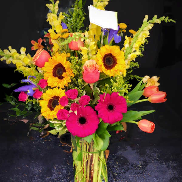Mixed bouquet with sunflowers, pink gerberas, roses, and tulips in a glass vase