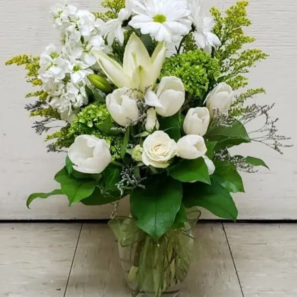 White floral arrangement in a clear glass vase with green accents