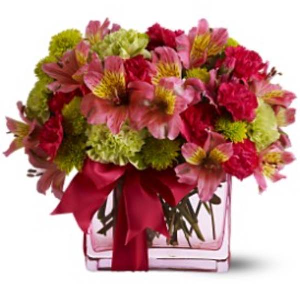 Bouquet of pink and red flowers in a clear square vase with a red ribbon