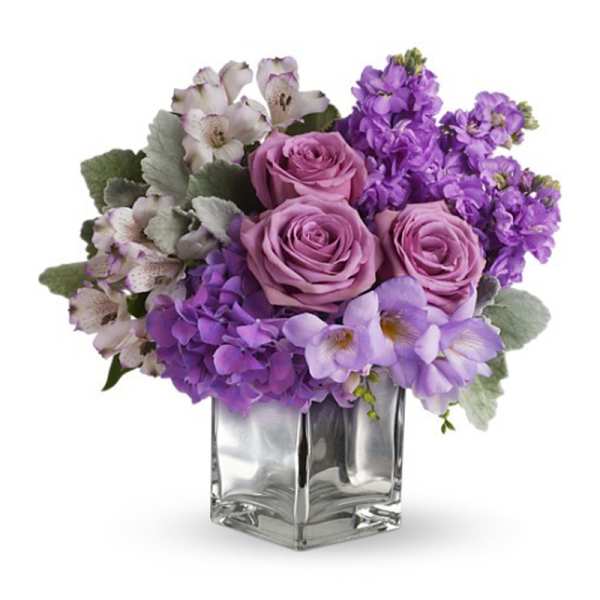 Purple roses and mixed lavender flowers in a clear glass vase