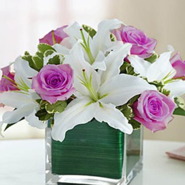White lilies and pink roses arranged in a clear square vase