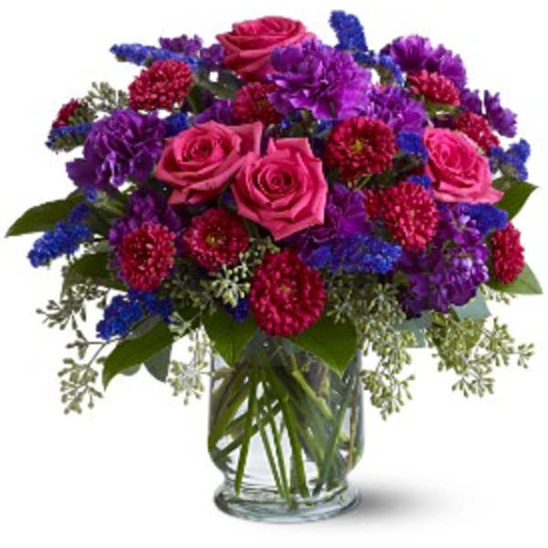 Bouquet of pink roses, purple blooms, and blue filler in a glass vase