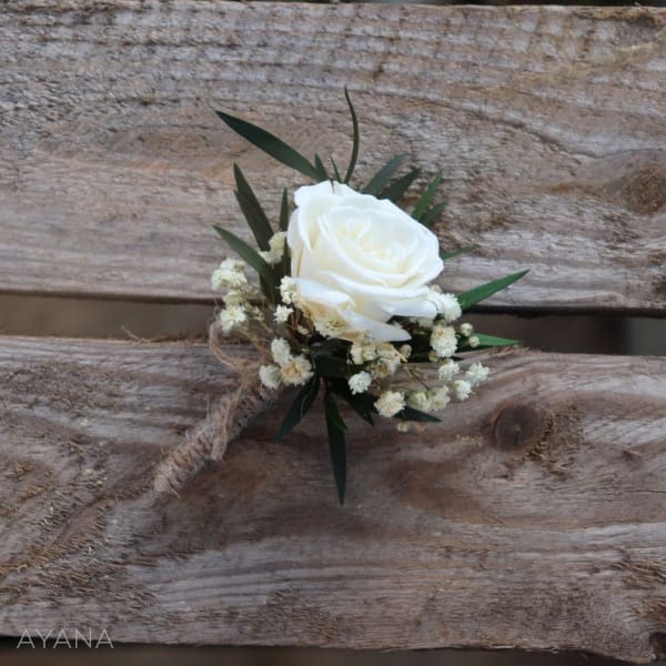 White rose boutonniere with small filler flowers and dark leaves
