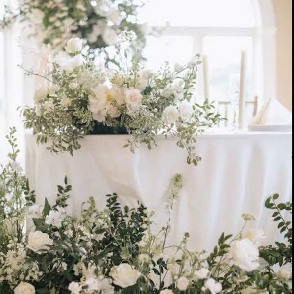 White floral arrangements with greenery on a draped table in a bright room