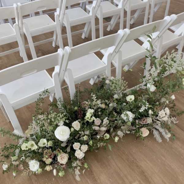 Low floral arrangement beside rows of white chairs