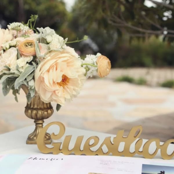 Peach and cream floral arrangement in a gold vase beside a gold guestbook sign