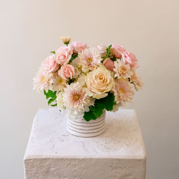 Low arrangement of blush roses, white hydrangeas, and soft pink mums in a white ribbed ceramic vase