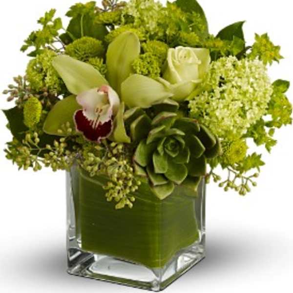 Green floral arrangement in a square glass vase with white orchids and roses