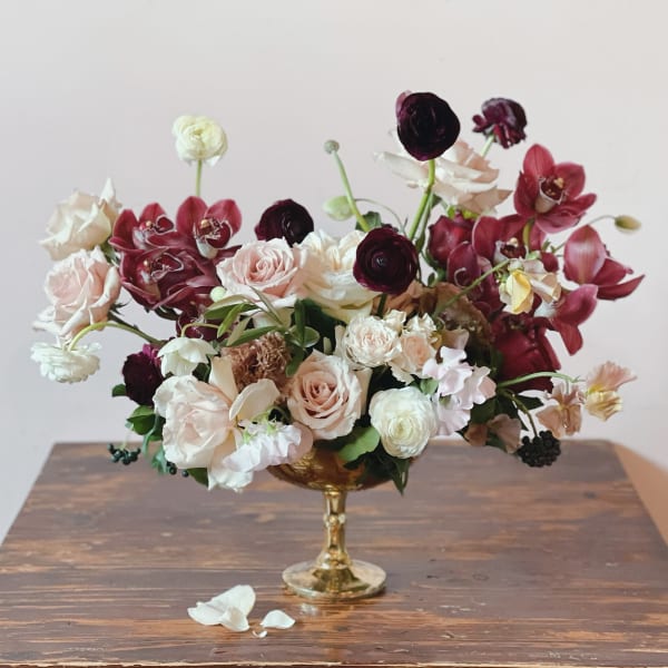 Mixed bouquet of blush, white, and burgundy flowers in a gold goblet vase
