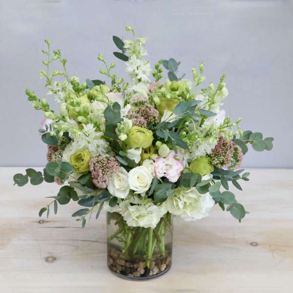 Round arrangement of white and green flowers with eucalyptus in a clear glass vase with stones.