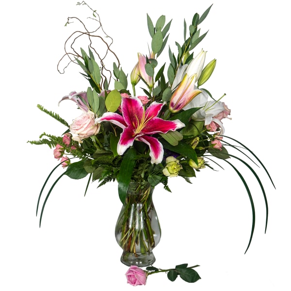Tall arrangement of pink lilies and roses in a clear glass vase with a single pink rose at the base