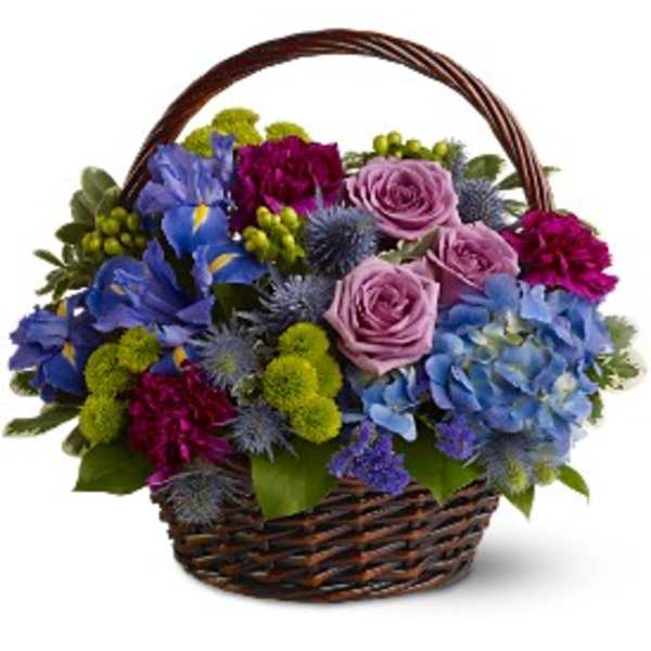 Basket arrangement of blue hydrangeas, purple roses, blue irises, and green button mums