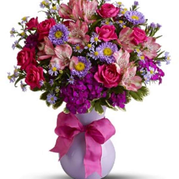 Bouquet of pink roses and mixed flowers in a lavender vase with a pink ribbon