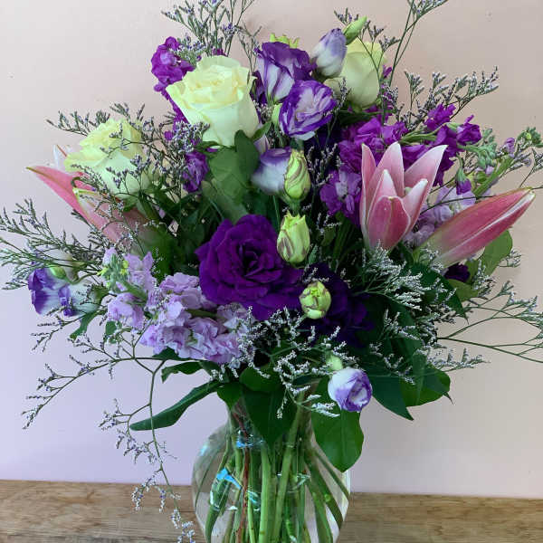 Purple and pink bouquet with roses and lilies in a glass vase