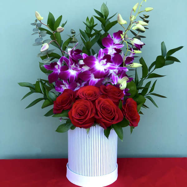 Red roses and purple orchids in a striped white box