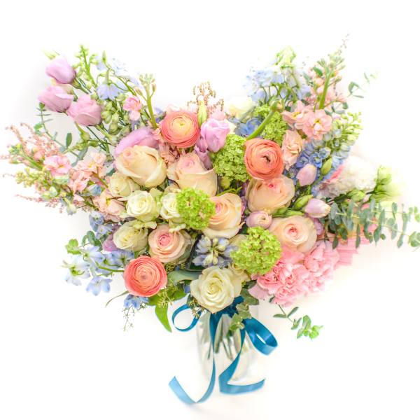 Pastel mixed flower bouquet with a blue ribbon in a clear vase