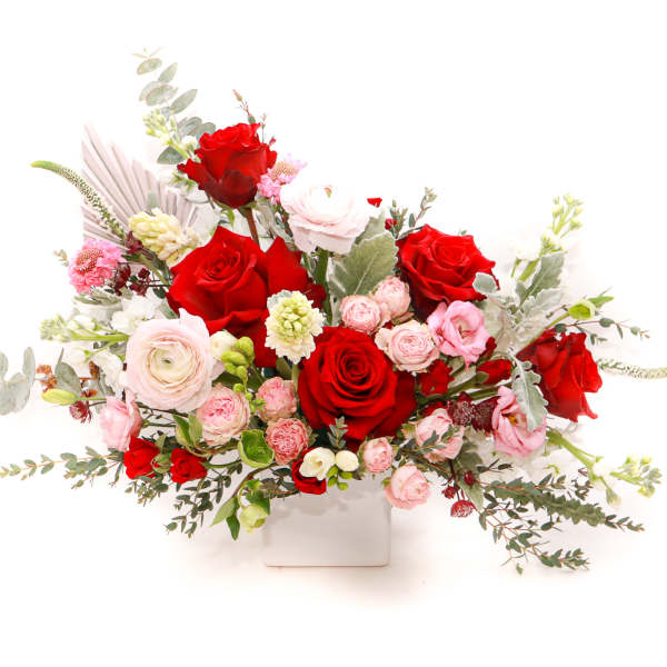 Red and pink rose arrangement in a white square vase