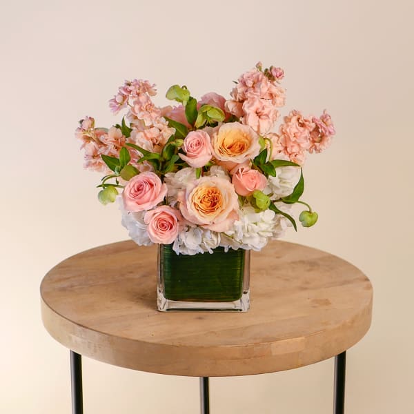 Pink and peach roses arranged with white blooms in a square glass vase