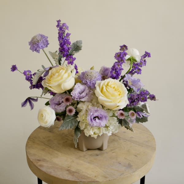 Pastel floral arrangement with yellow roses and purple blooms in a small vase