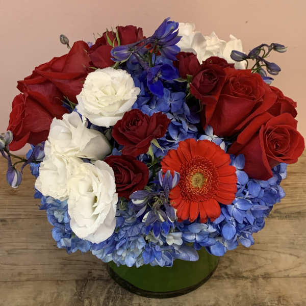 Red and white roses with blue hydrangeas and an orange gerbera daisy in a green vase