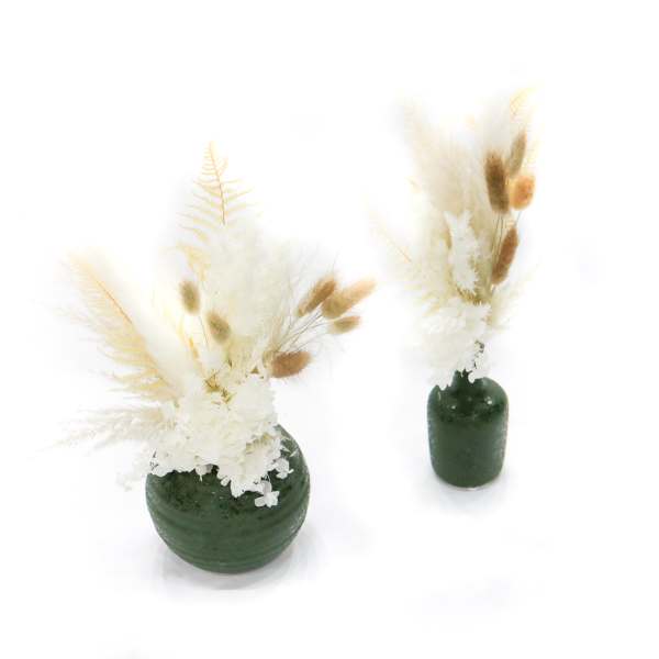 Two dried floral arrangements in dark green vases on a white background