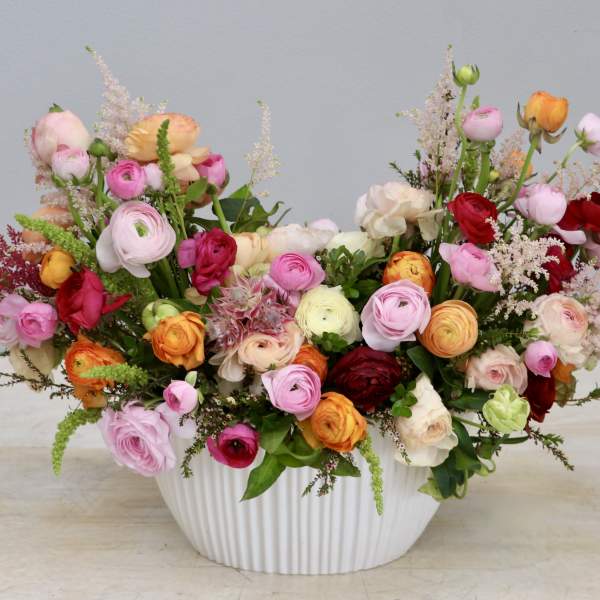 Low white ceramic bowl filled with pink, red, orange, and cream ranunculus arrangement