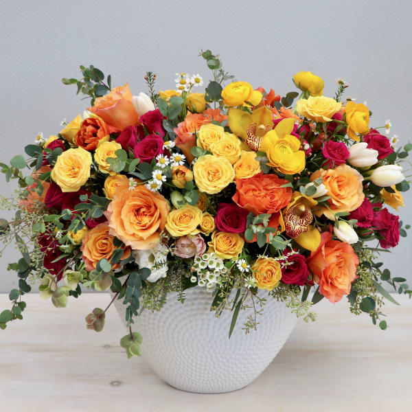 Large arrangement of yellow, orange, and red roses with mixed blooms in a white textured ceramic bowl