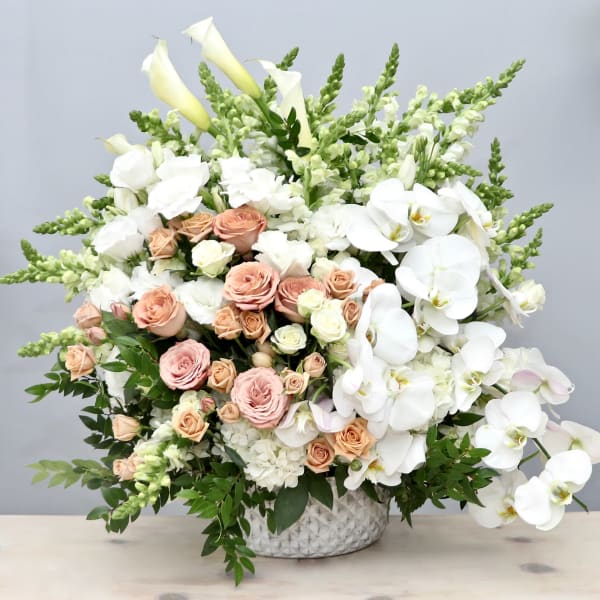 Large arrangement of white orchids, calla lilies, and peach and cream roses in a white vase