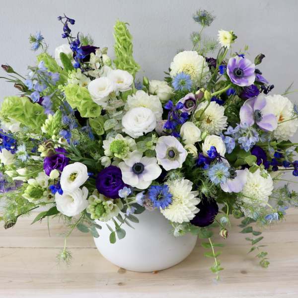 Mixed white, blue, and purple flowers in a white bowl vase