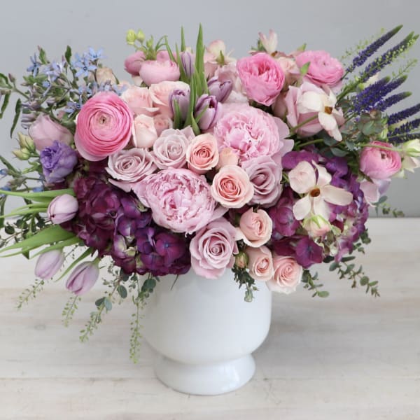 Low pink and purple flower arrangement with roses and peonies in a white ceramic vase.