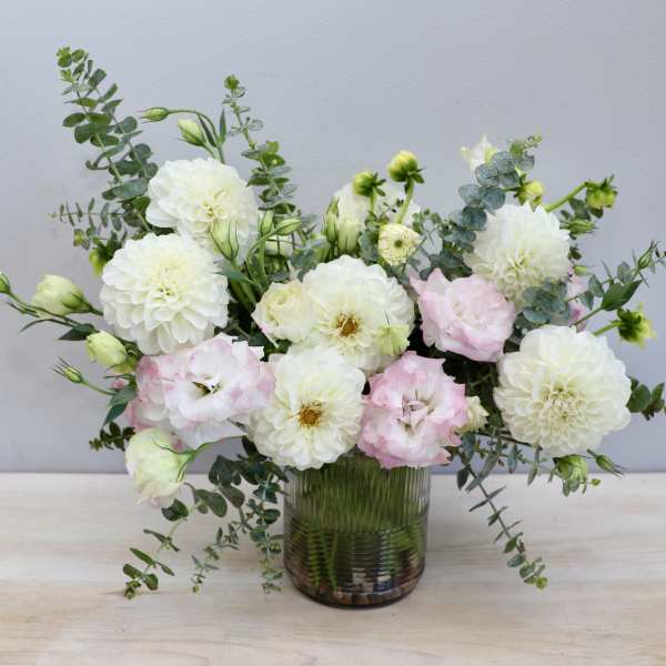 Low glass vase of white dahlias and pale pink lisianthus with airy greenery.