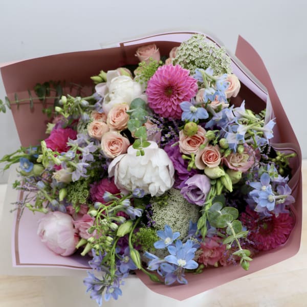 Mixed bouquet of pink, purple, blue, and white flowers wrapped in pink paper