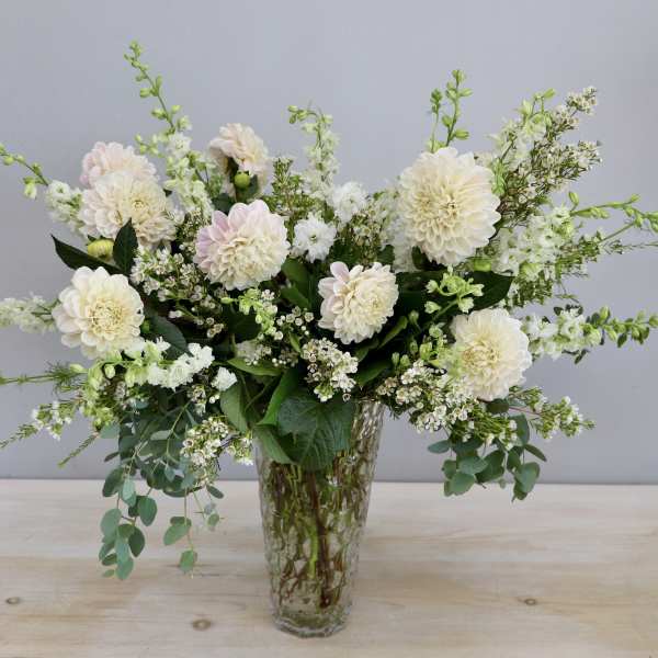 Tall arrangement of cream dahlias and white flowers in a clear textured glass vase