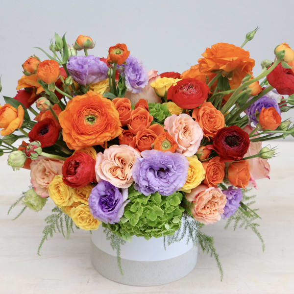 Low white vase filled with bright orange, red, yellow, and purple flowers in a wide arrangement