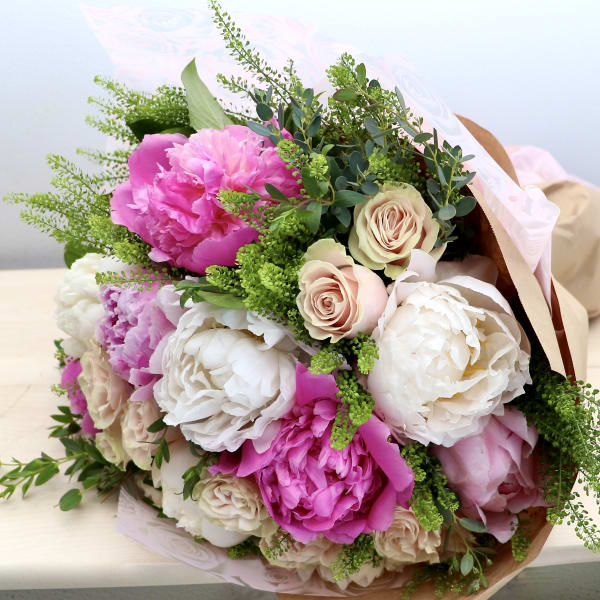 Hand-tied bouquet of pink peonies and cream roses wrapped in kraft paper