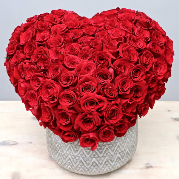 Heart-shaped arrangement of red roses in a patterned white ceramic pot