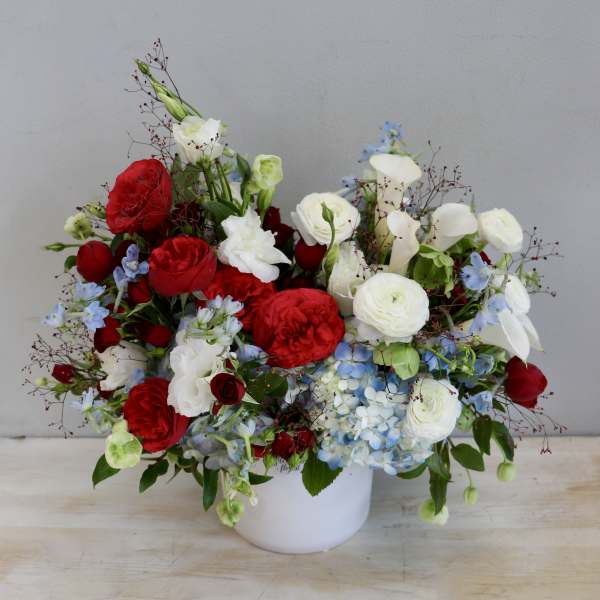 Red, white, and blue flower arrangement in a white ceramic vase