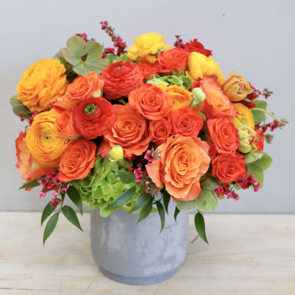 Bright orange and yellow flower arrangement in a gray vase