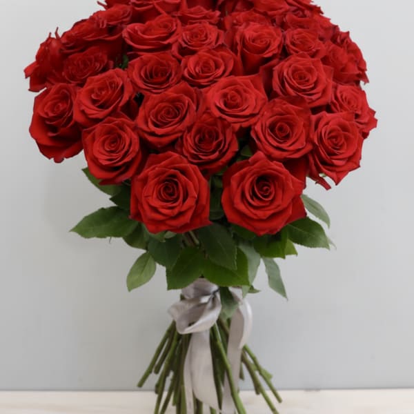 Large hand-tied bouquet of red roses with long stems tied by a silver ribbon