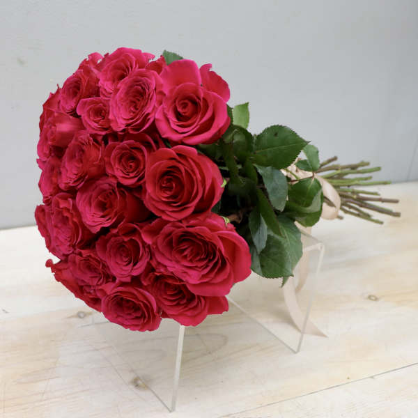 Hand-tied bouquet of hot pink roses with long stems and ribbon lying on a clear stand.