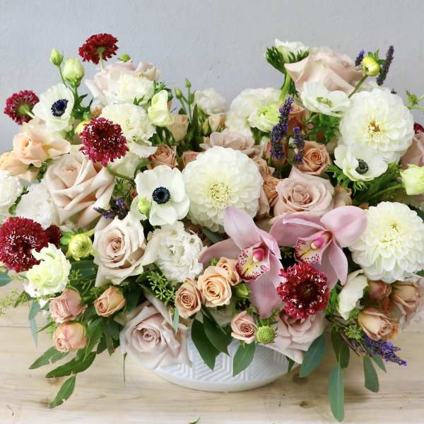 Mixed bouquet of blush roses, white blooms, and pink orchids in a white bowl vase